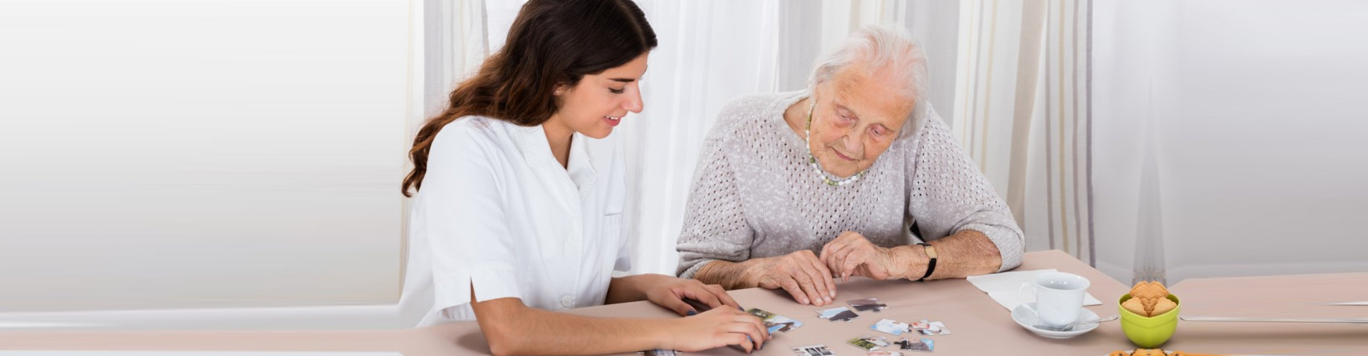 elder woman playing jigsaw puzzle on table with her caregiver